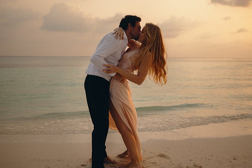 Romantic couple sharing a kiss on a tropical island at sunset during a luxury holiday