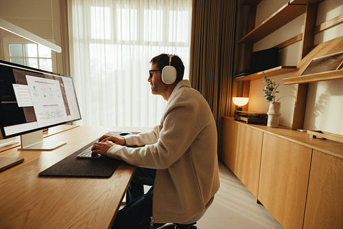 Man works at computer with headphones in a bright office