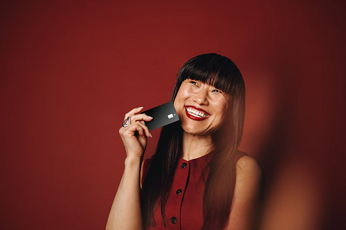 Woman holding banking card and smiling in red studio portrait