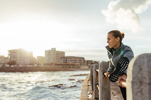 Healthy woman stretching on railing at seaside road