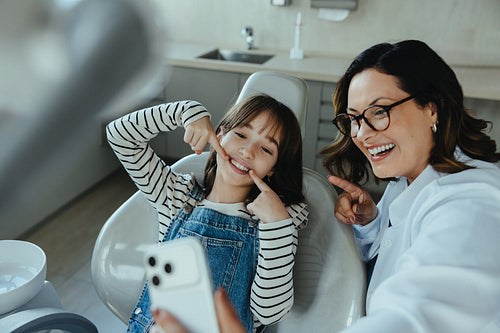 Dentist and child take selfie and point to healthy teeth in clinic
