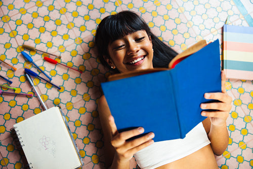 Smiling girl reading book while lying on colorful patterned floor