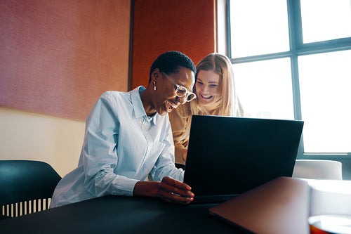 Two diverse women discussing ideas while working together on a laptop in office