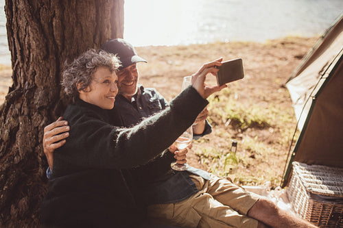 Mature couple camping near a lake taking selfie