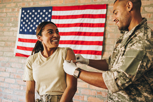 Happy servicewoman smiling at the military nurse after vaccinati