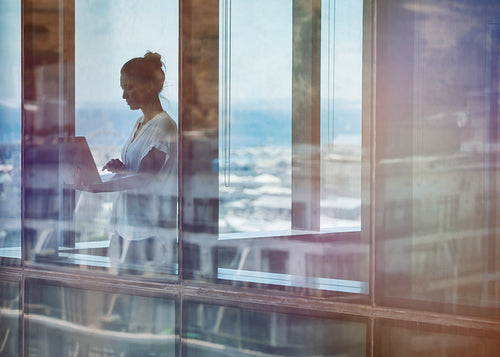 Businesswoman standing inside office building and using laptop