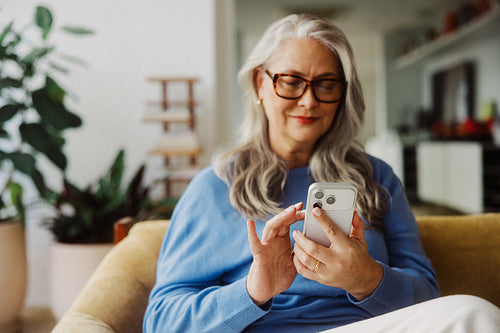 Senior woman uses a smartphone while relaxing at home