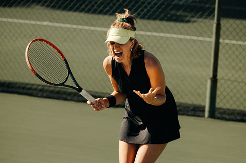 Woman shouting while playing tennis on outdoor court, holding a racket