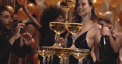 Woman dancing around a pyramid of champagne glasses with friends at a party