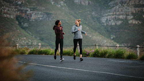 Two women athletes running on road