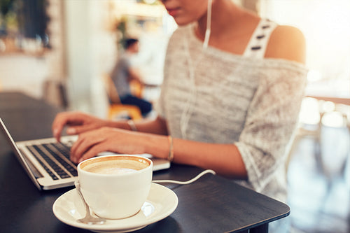 Cap of coffee on cafe table with a woman using laptop