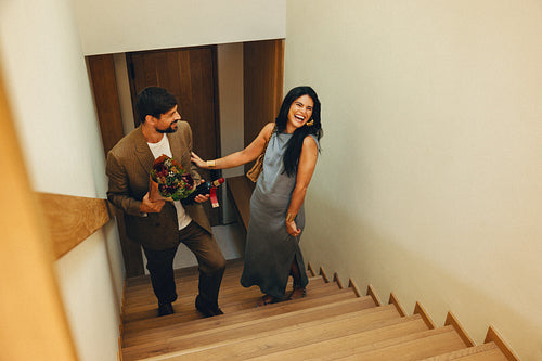 Man presenting flowers and wine to smiling woman on a staircase