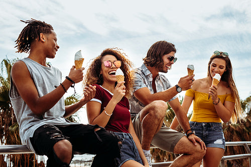 Smiling young friends eating ice-cream outdoors