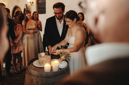 Bride and groom cutting their wedding cake surrounded by family and friends
