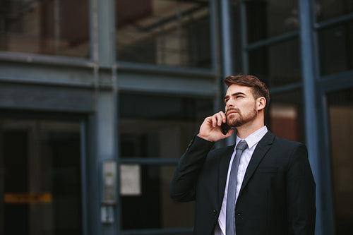 Businessman walking out of office and talking over mobile phone