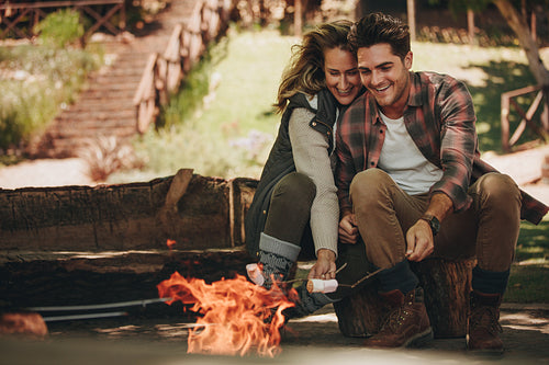 Smiling couple roasting sweets on bonfire