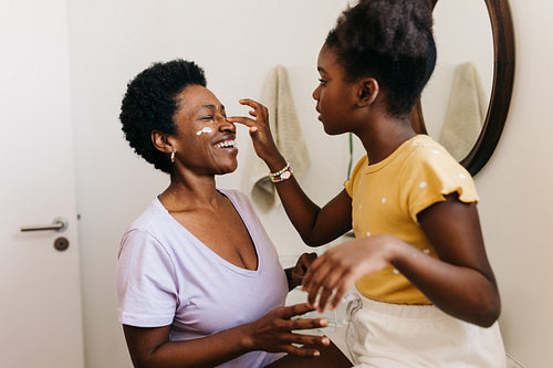 A mother and daughter's morning skincare routine: Girl putting face cream on her mom