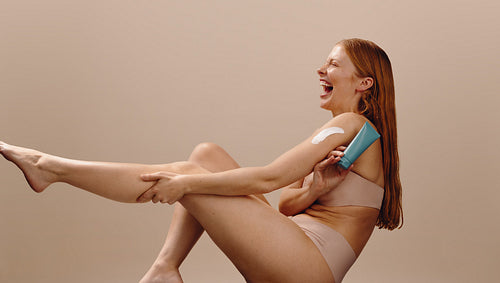 Woman applying moisturizer to arm while laughing