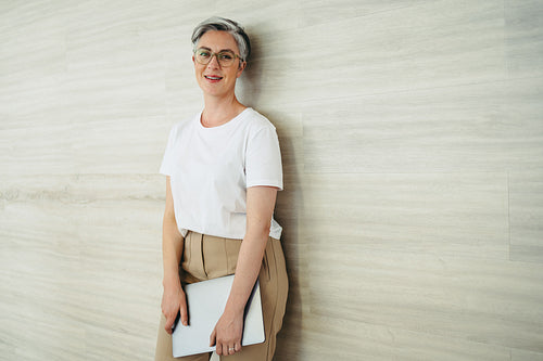 Happy businesswoman standing against a wall in a modern office