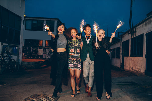Group of friends walking with sparklers on road in evening