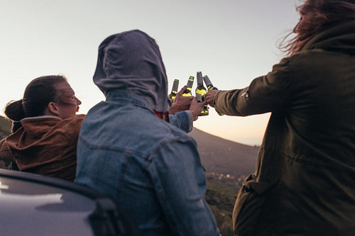 Rear view of friends toasting beer sitting outdoors