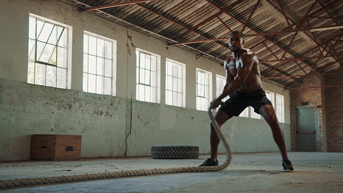 Athletic man exercising with battle rope in gym