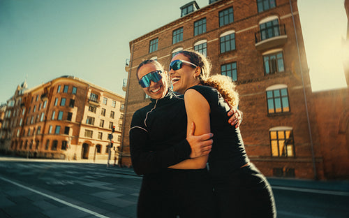 Running friends hugging and laughing outdoors after a social fitness club meetup