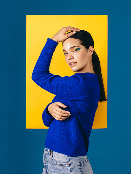 Confident young woman looking at the camera with striking graphic eyeliner on her face, standing in front of a geometric shape