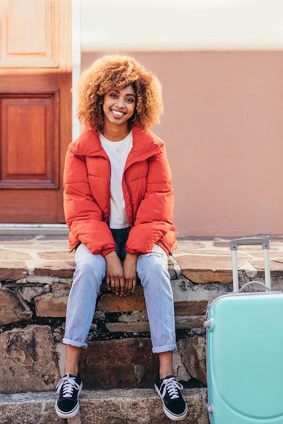 Smiling female traveller sitting outdoors with her luggage