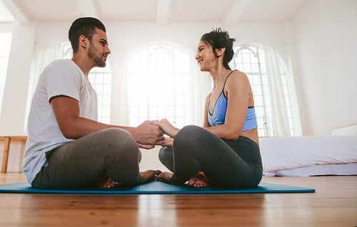 Couple sitting together on the yoga mat holding hands