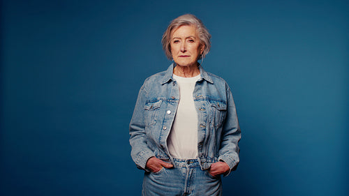 Smiling senior woman in denim jacket laughs on blue studio background