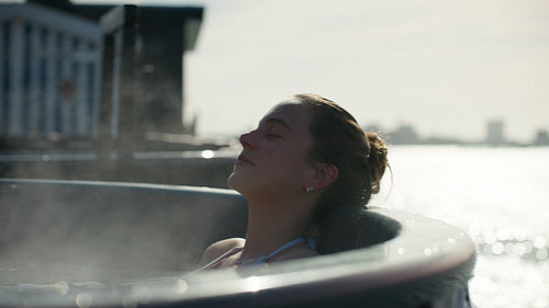The woman enjoys a peaceful morning soak in an outdoor spa by the waterfront