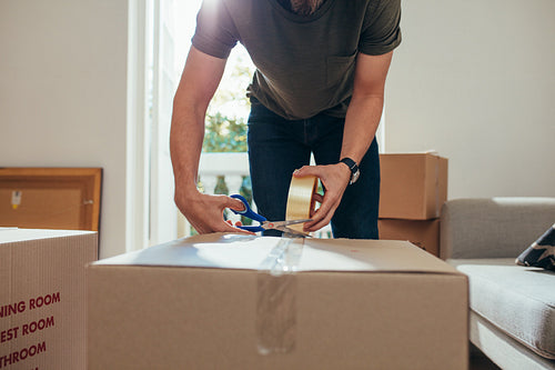 Man packing his household stuff in packing boxes and sealing them with adhesive tape.