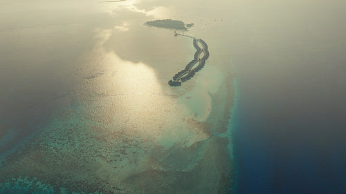 Aerial drone shot of a luxurious tropical island resort with overwater bungalows at sunrise