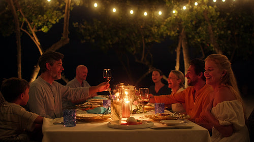Joyful family and friends enjoying an illuminated outdoor dinner at a beautiful island resort