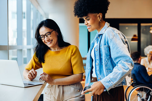 Two women collaborate at laptop in office.