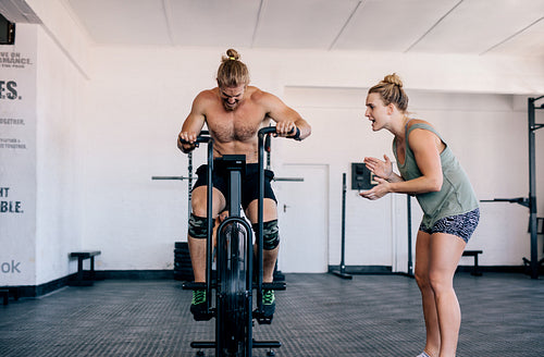Personal trainer motivating man exercising on gym bike 