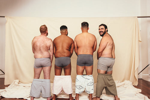 Four men standing in a studio with their shorts dropped down