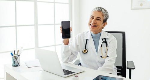 Experienced doctor recommending a smartphone while sitting in her office