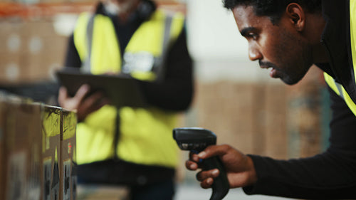 Warehouse trainee scans boxes with a barcode scanner under supervision of his manager