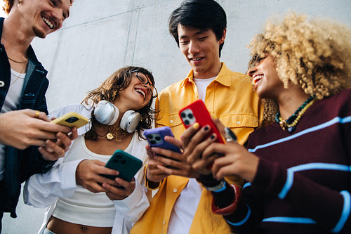 Friends laughing together while sharing smartphones