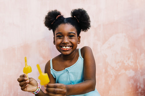 Happy afro-hared girl enjoying delicious flavoured ice lollies