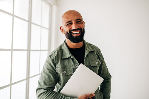 Happy business man standing in an office holding a laptop