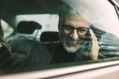 Smiling senior businessman making phone call in cab
