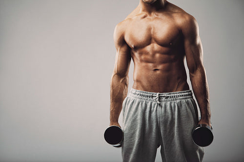 Fitness male model with dumbbells on grey background