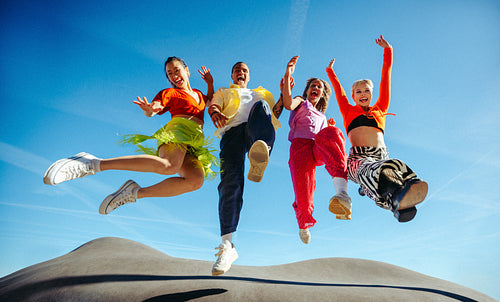 Friends jumping together outdoors under a blue sky in a joyful celebration