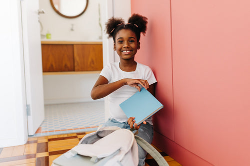 Afro school girl packing her bag with books for primary school