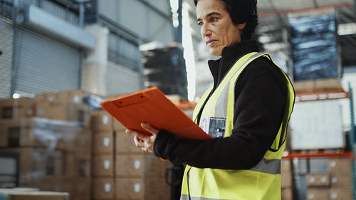 Inventory management in a distribution center: Female worker assessing the stock in a warehouse as she reads a file
