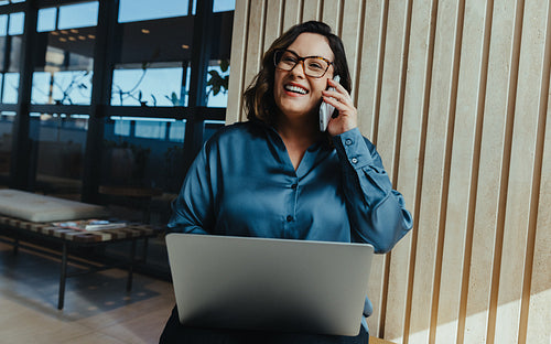 Business woman talks on phone while using laptop in modern office