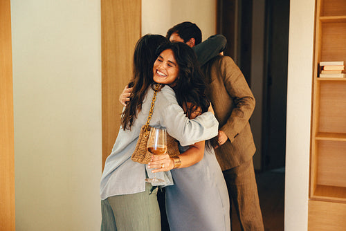 Friends joyfully hugging during a dinner party at someone's home